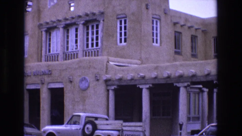 1973 New Mexico home-movie frame showing part of the Federal Building sign, upper multi-pane windows, white columns, and a light-colored pickup truck parked in front.