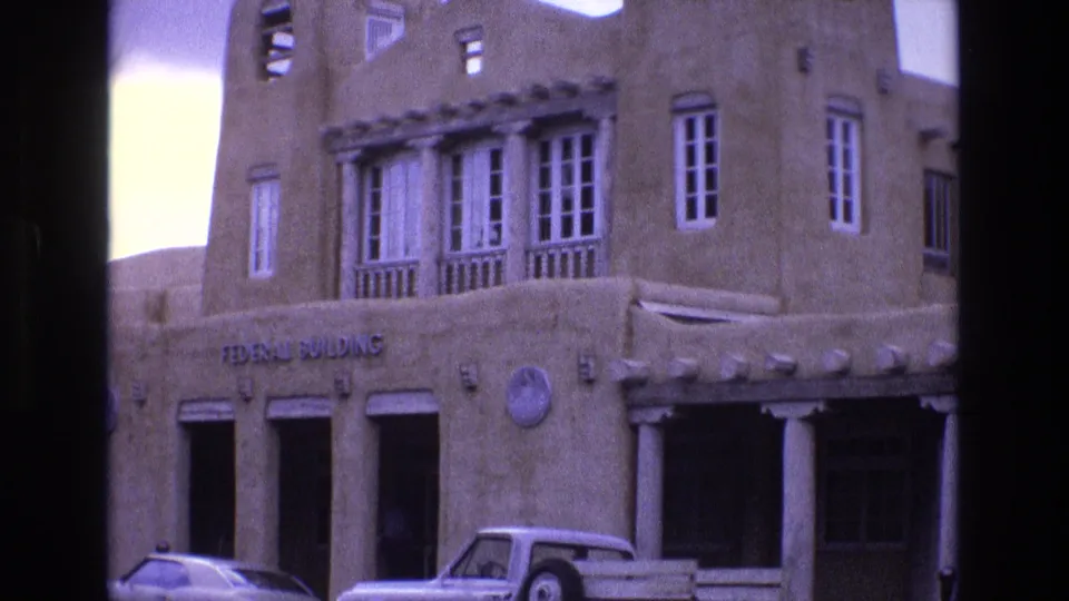 1973 New Mexico frame showing the Federal Building sign across an adobe-style facade, a row of white columns, upper windows, and a pickup truck parked below.