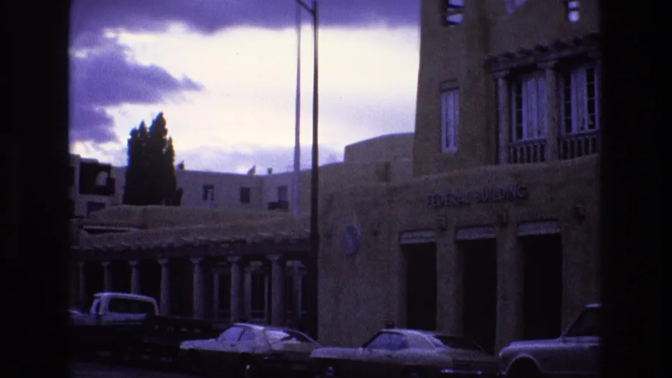 1973 New Mexico frame with the Federal Building at the right edge, parked cars below, and a purple-tinged cloudy sky above the street.