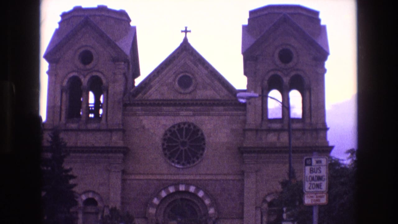 Church facade with twin bell towers, rose window, cross, and bus loading zone sign.