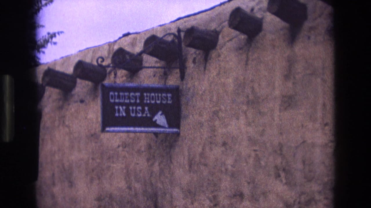 1973 New Mexico home-movie frame with a close angled view of the adobe facade, roof beams, and readable "Oldest House in USA" sign.