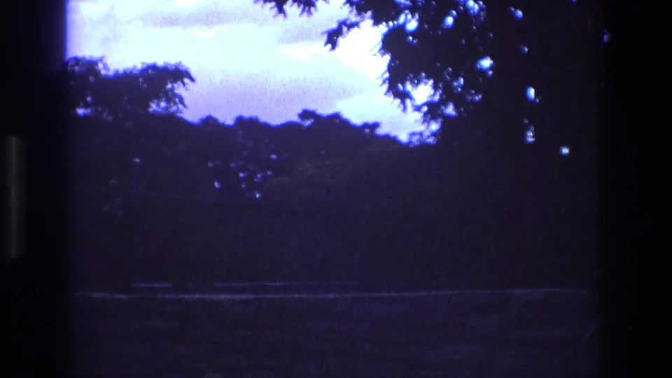 1973 New Mexico 8mm frame with a dark vertical window or film edge, silhouetted trees, blue-purple dusk sky, and a faint path crossing the lower scene.