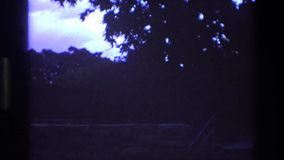 1973 New Mexico 8mm frame showing silhouetted trees, a low-light walkway, and an angled stair or railing shape emerging in the lower right.
