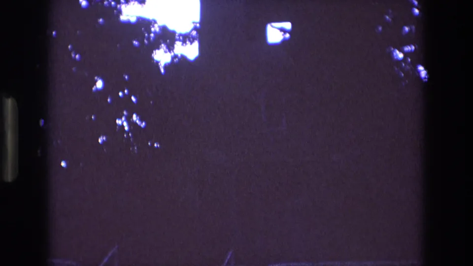 1973 New Mexico 8mm frame showing a dark, purple-tinted sky with overexposed light flares and silhouetted tree branches before the building is revealed.