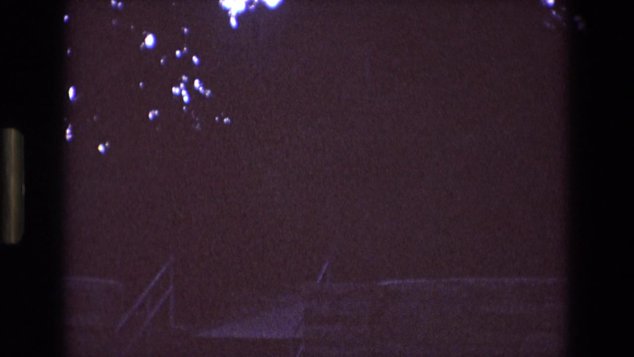 1973 New Mexico 8mm frame with a dark purple sky, faint tree branches, and the upper roofline of a large institutional-looking building entering the lower frame.