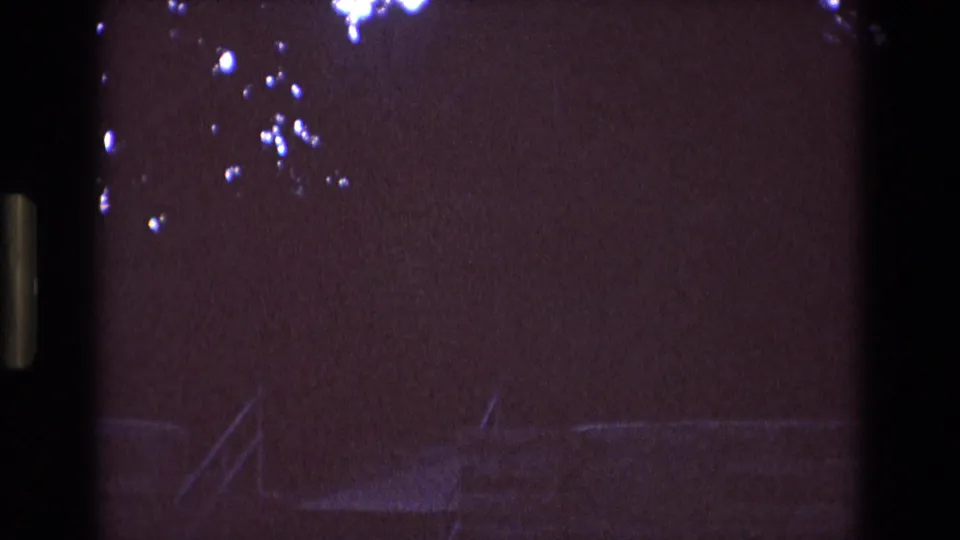 1973 New Mexico 8mm frame with a dark purple sky, faint tree branches, and the upper roofline of a large institutional-looking building entering the lower frame.