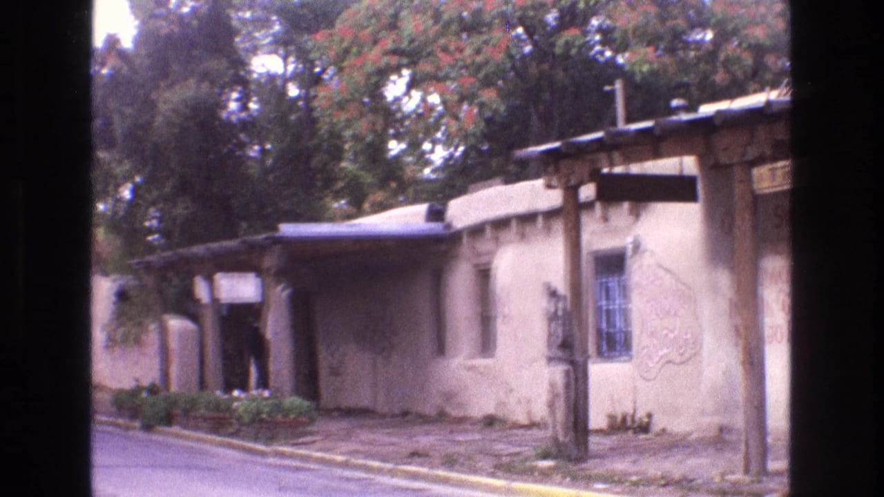 Adobe-style building beside a road with a barred window, porch, and painted wall lettering.