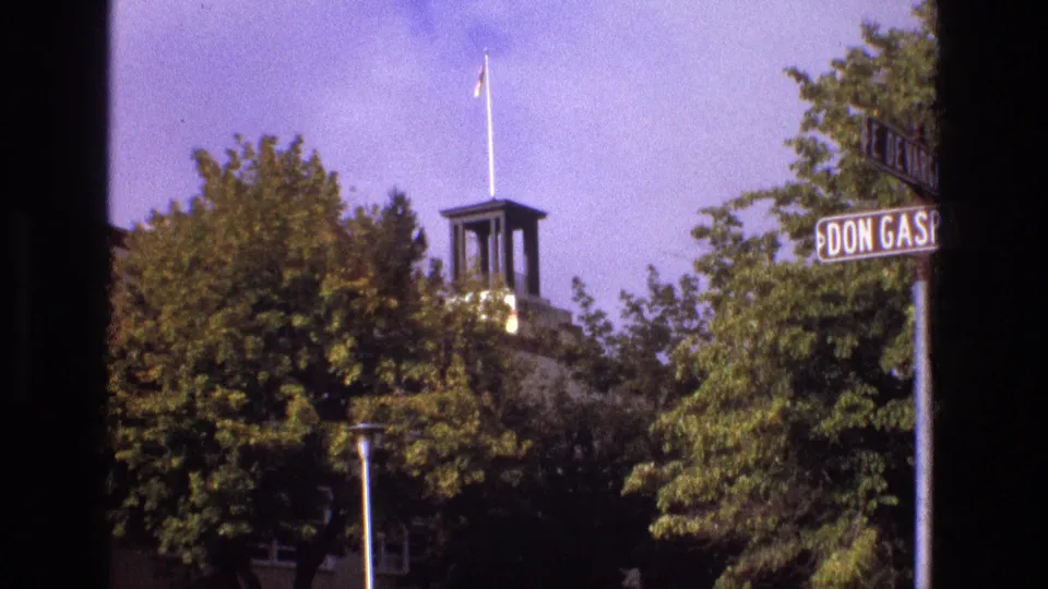 1973 New Mexico 8mm frame showing a Don Gaspar street sign, dense green trees, and a partly obscured historic-looking building with a small tower and flagpole.