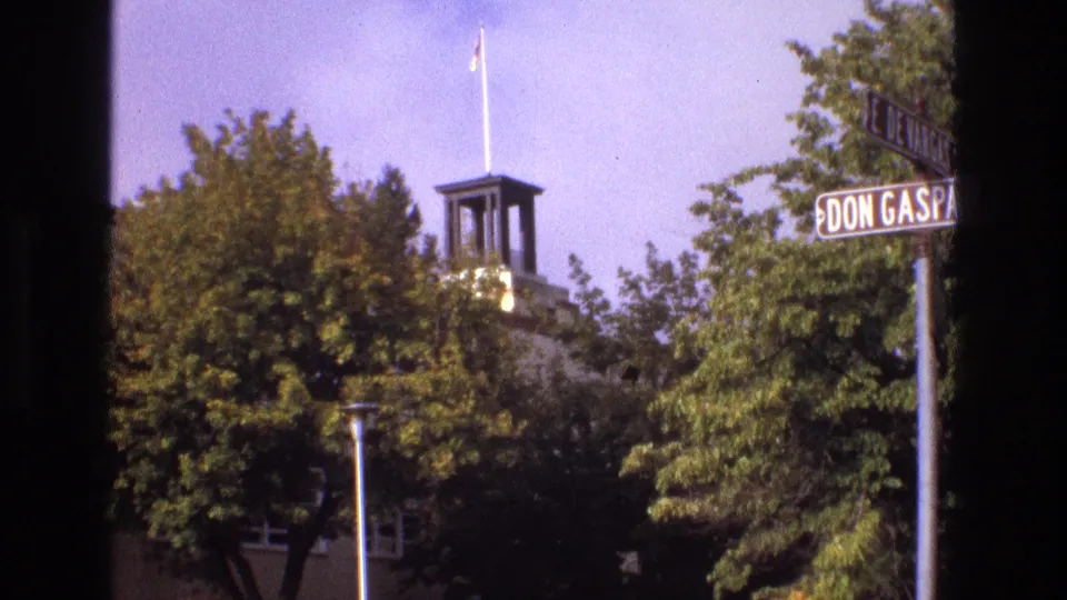 1973 New Mexico street-corner view with Don Gaspar signage, leafy trees, a small tower, and a flagpole visible above the roofline.