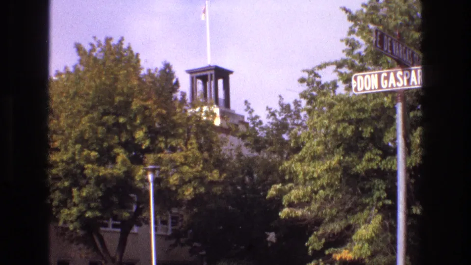 1973 New Mexico 8mm frame of the Don Gaspar and E. De Vargas intersection area, with foliage obscuring much of a building topped by a small tower.