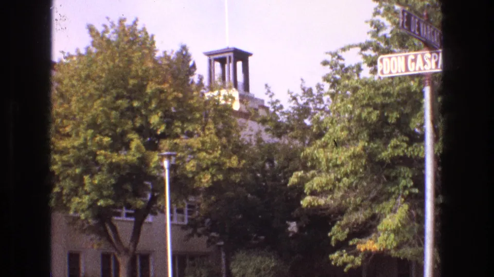 Final 1973 New Mexico frame holding on a Don Gaspar street sign, dense roadside trees, and a partly hidden building with a small tower and flagpole.