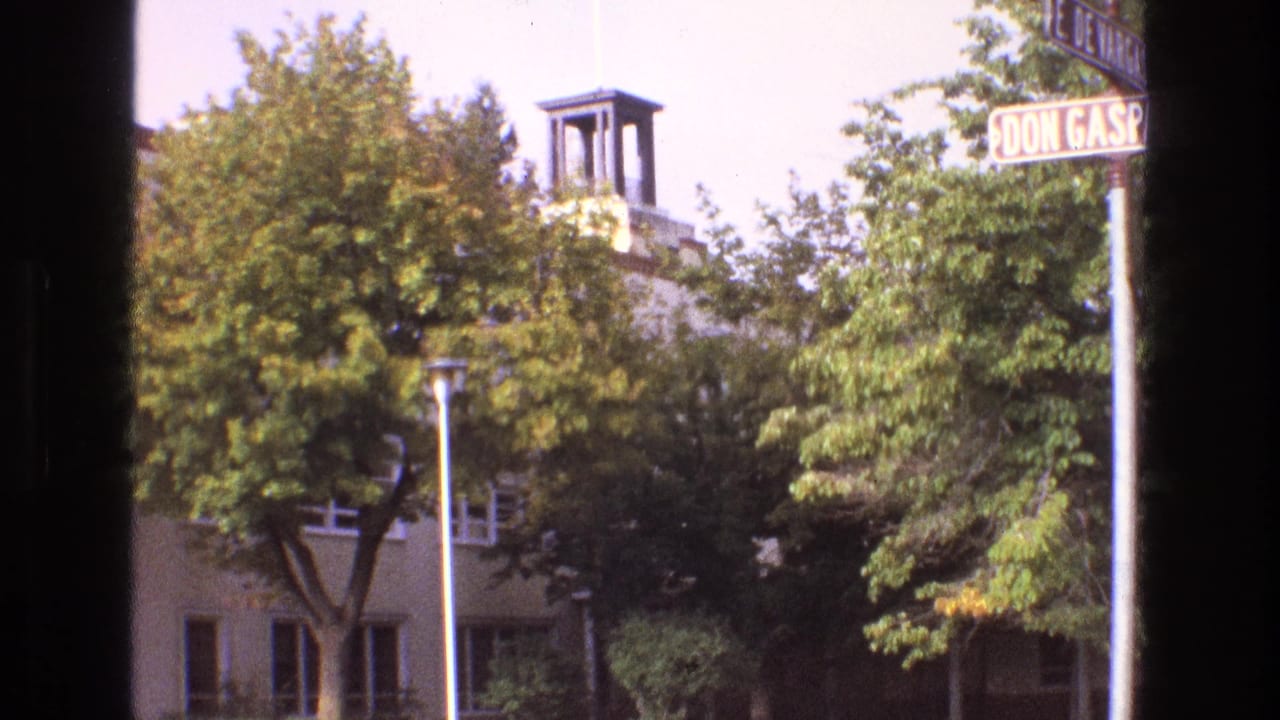 1973 New Mexico 8mm frame showing Don Gaspar Avenue signage partly cropped above trees, with a light-colored building and small bell tower behind foliage.