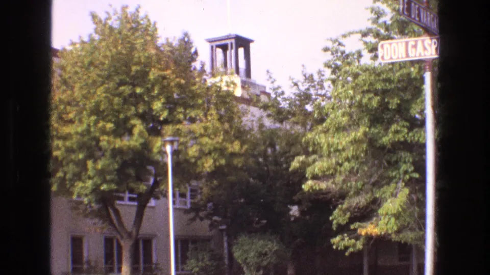 1973 New Mexico 8mm frame showing Don Gaspar Avenue signage partly cropped above trees, with a light-colored building and small bell tower behind foliage.