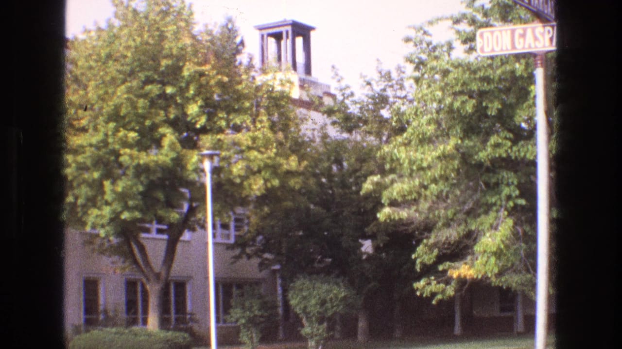 1973 New Mexico frame with a cropped Don Gaspar Avenue street sign, dense green trees, and a small bell tower rising from a light building in the background.