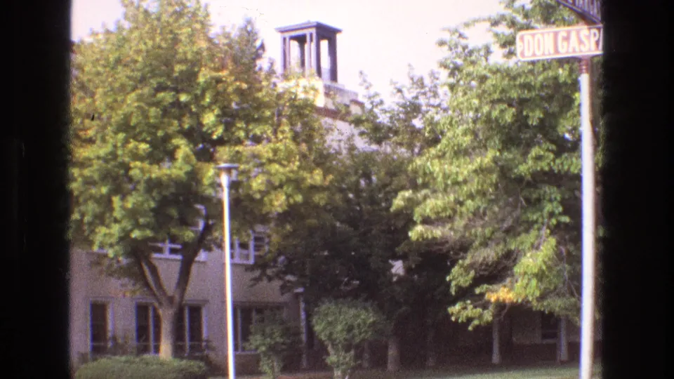 1973 New Mexico frame with a cropped Don Gaspar Avenue street sign, dense green trees, and a small bell tower rising from a light building in the background.