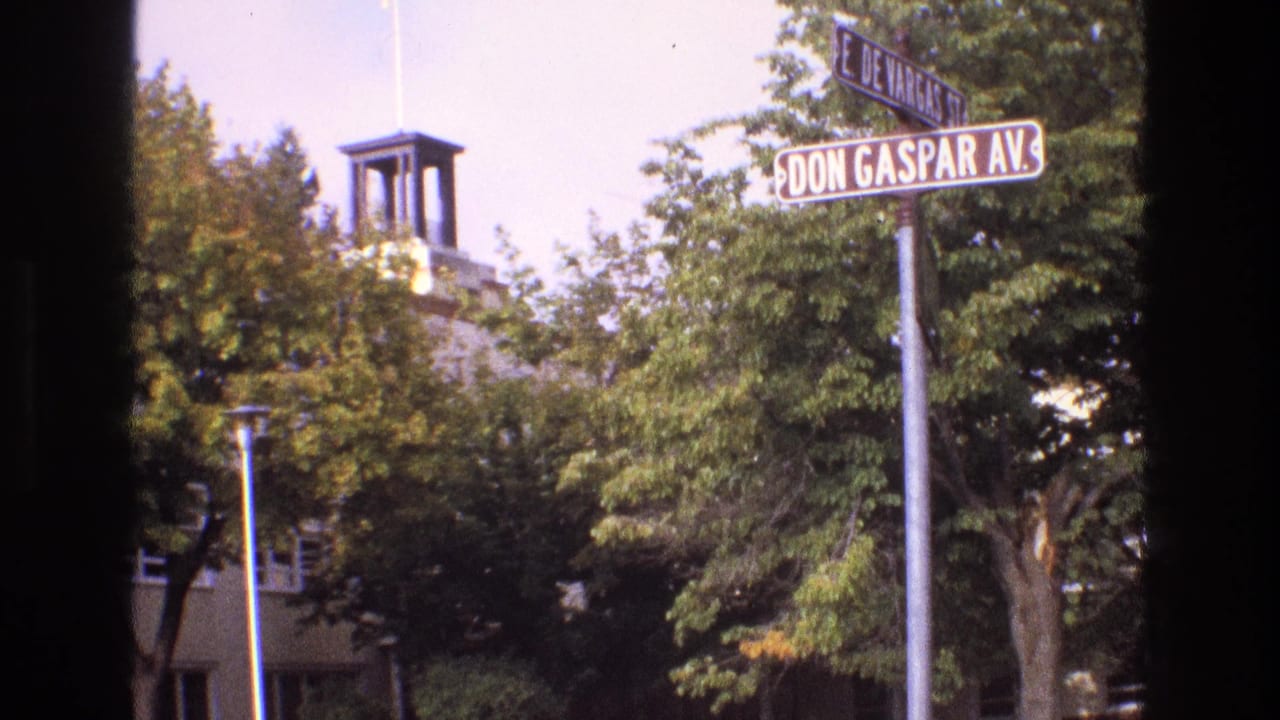 1973 New Mexico 8mm frame showing Don Gaspar Avenue and East De Vargas Street signs near leafy trees and a towered building, with dark film-edge obstruction at the sides.