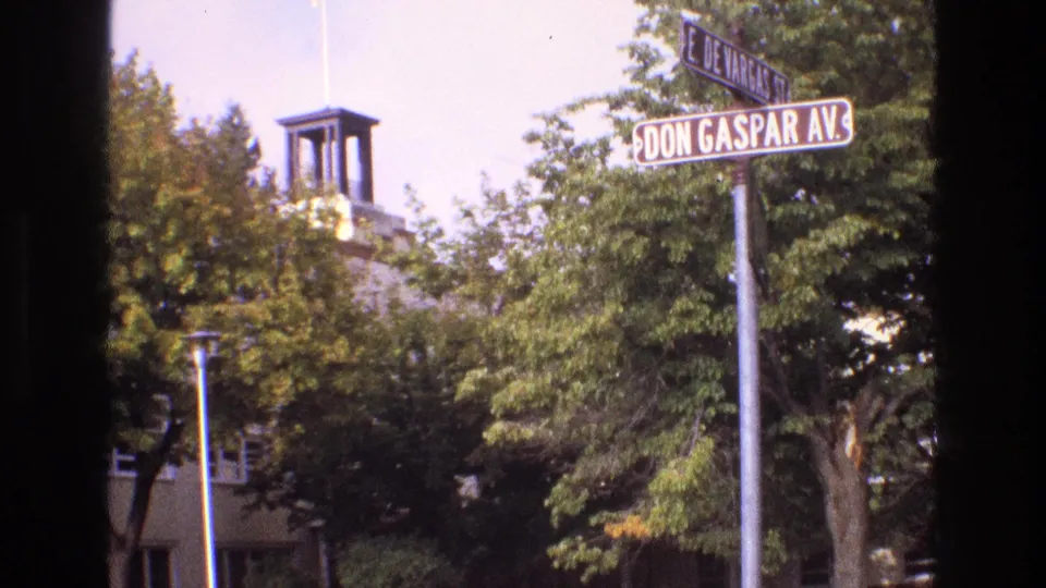 1973 New Mexico 8mm frame showing Don Gaspar Avenue and East De Vargas Street signs near leafy trees and a towered building, with dark film-edge obstruction at the sides.