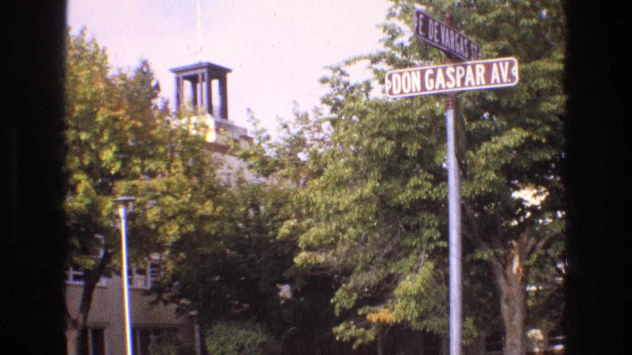 Street-corner signs and trees with a towered building partly visible behind them.