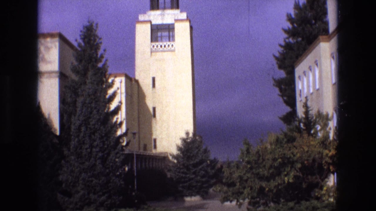 1973 New Mexico 8mm frame showing a pale towered building with geometric detailing, lower wings, evergreen trees, and a color-shifted sky.