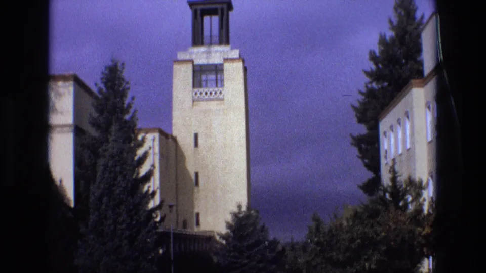 1973 New Mexico 8mm frame showing the towered pale building, a row of windows on a side wing, dense trees, and small-gauge film softness.