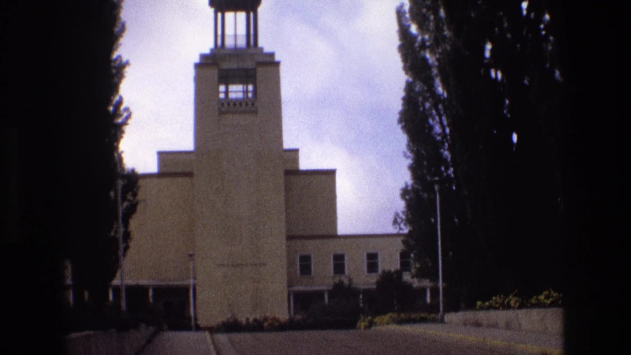 Centered exterior view of a tan towered building with trees and landscaping.