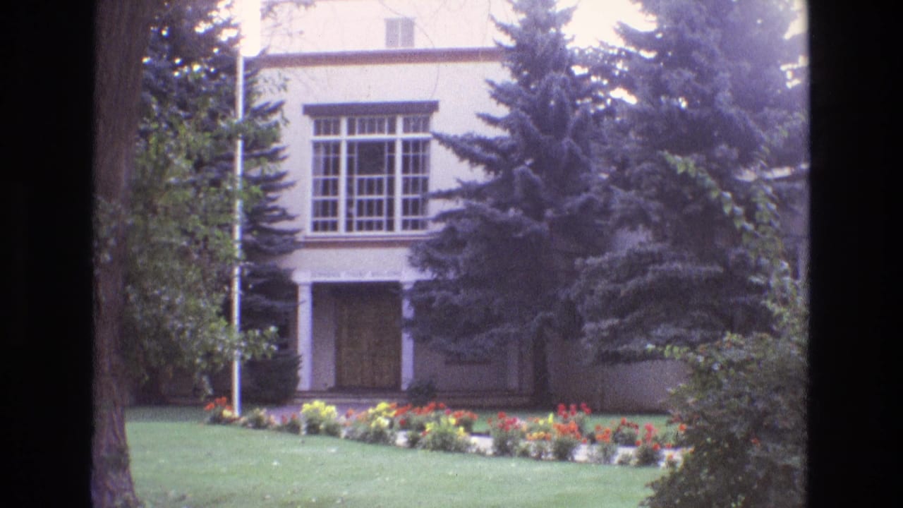 Similar exterior view of a stucco building with evergreens and flowers.