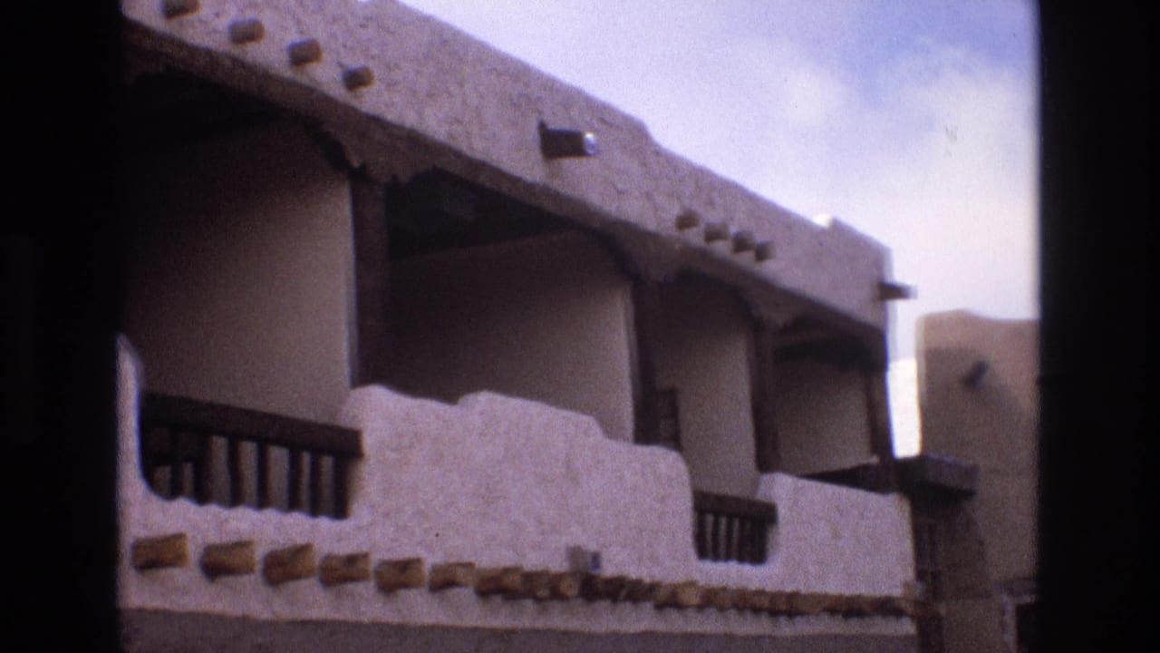 Balcony facade with stucco walls, roof beams, and shadowed openings.