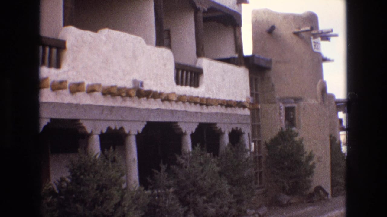 Southwestern-style building exterior with balcony, columns, beams, and shrubbery.
