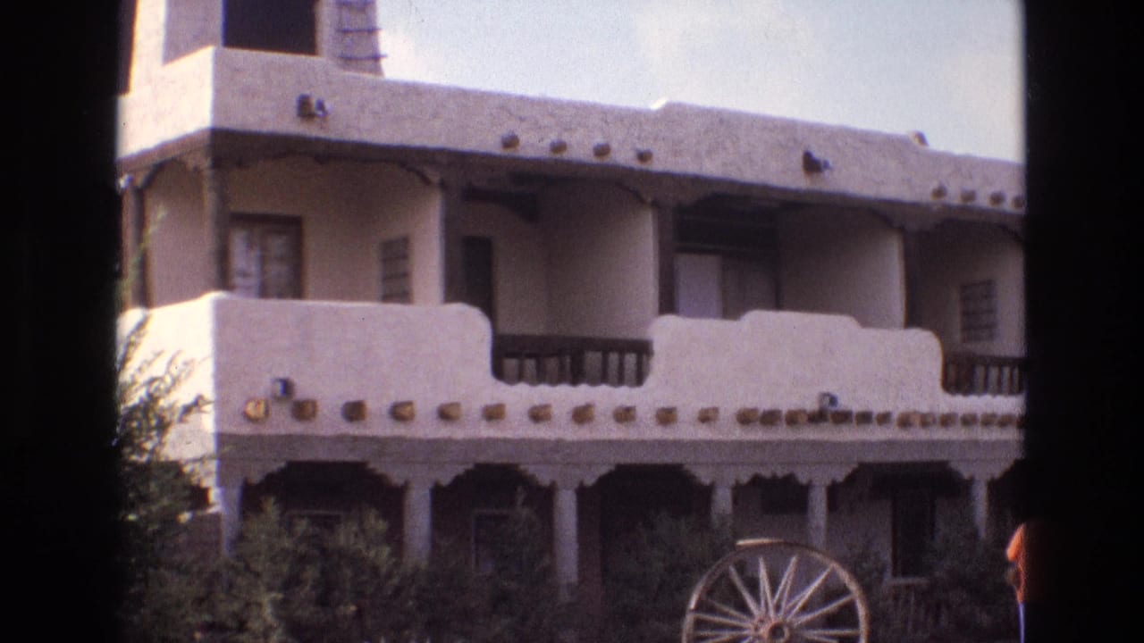 Stucco building facade with balcony railings, shrubs, and a wagon wheel.