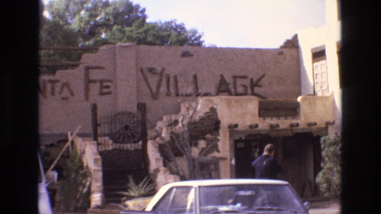 Santa Fe Village sign on adobe-style building with a man near parked cars.