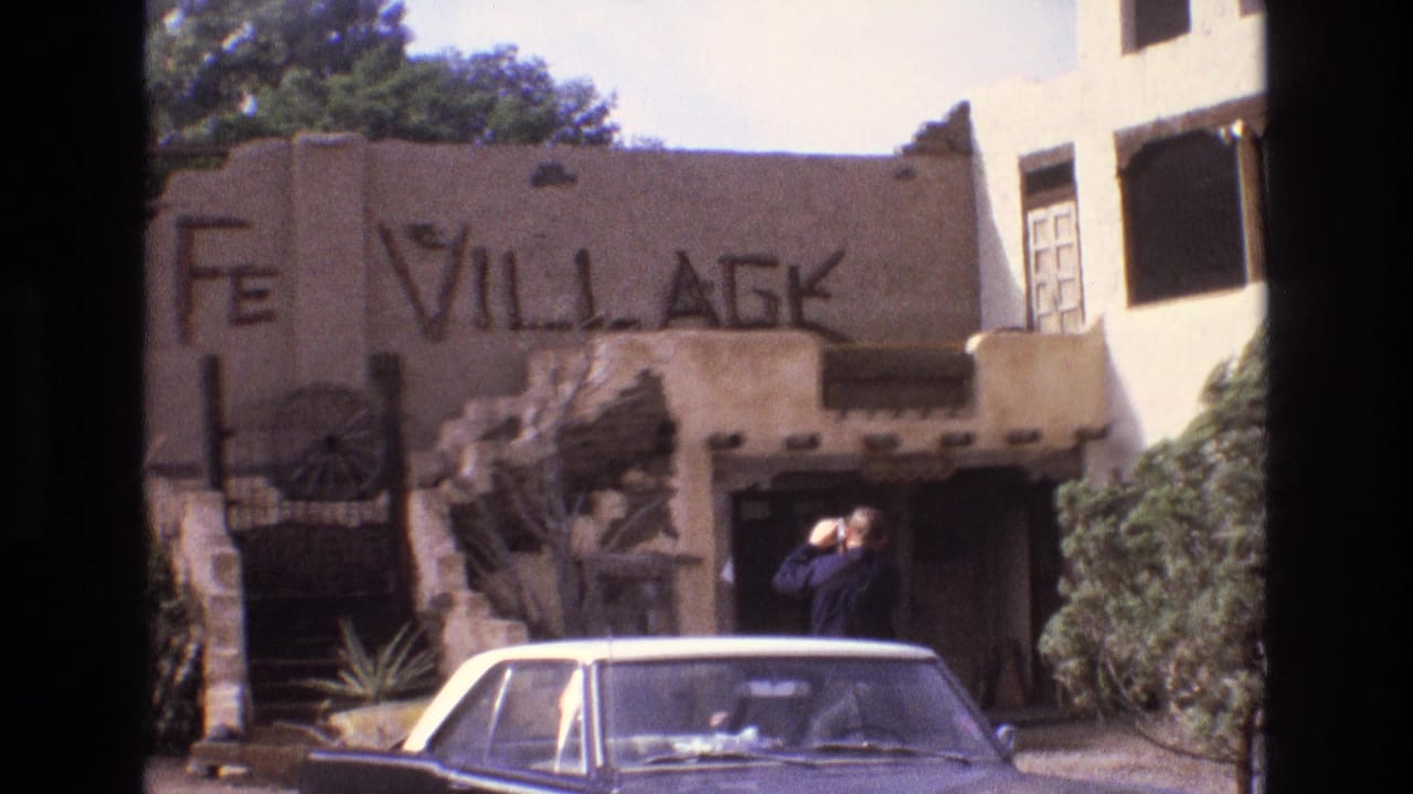 Man raises a camera near the entrance of a rustic Santa Fe Village building.