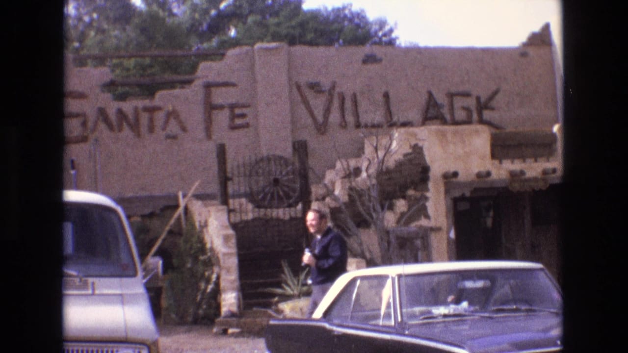 Man near the Santa Fe Village entrance with classic cars and an adobe-style facade behind him.