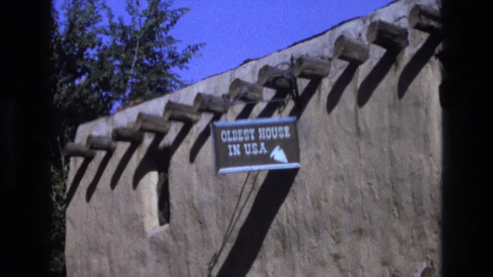1973 New Mexico 8mm frame showing a weathered adobe wall with projecting beams and a sign reading Oldest House in U.S.A.