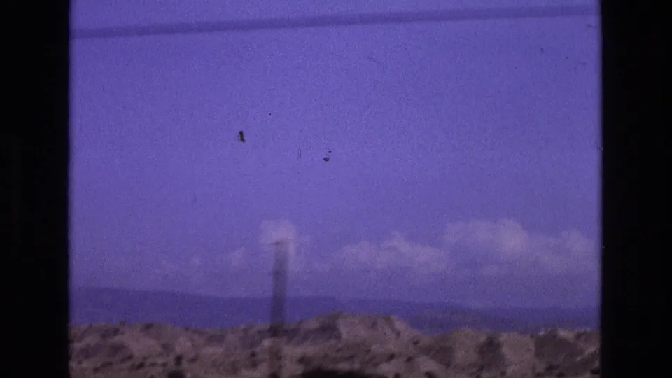 A soft purple-tinted transition frame from the same 8mm clip shows rough ground, distant hills, clouds, and a narrow vertical post or tower-like form.