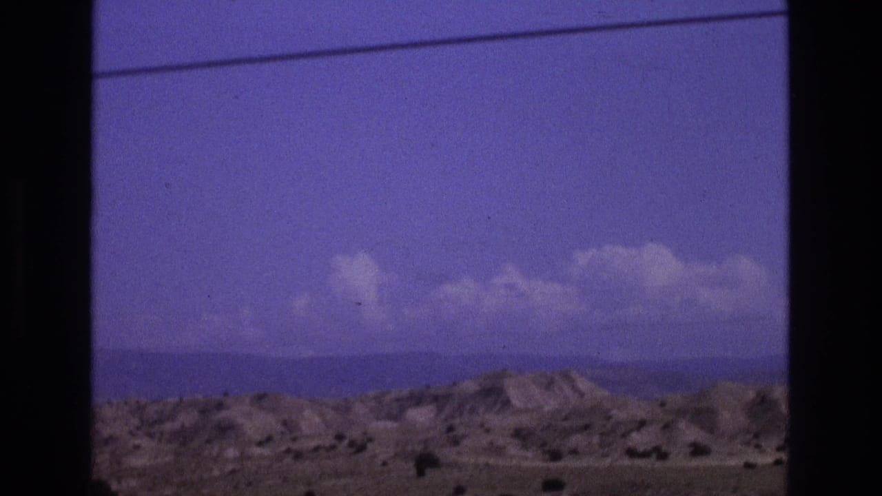 Arid hills and clouds with a power line crossing near the top of the frame.