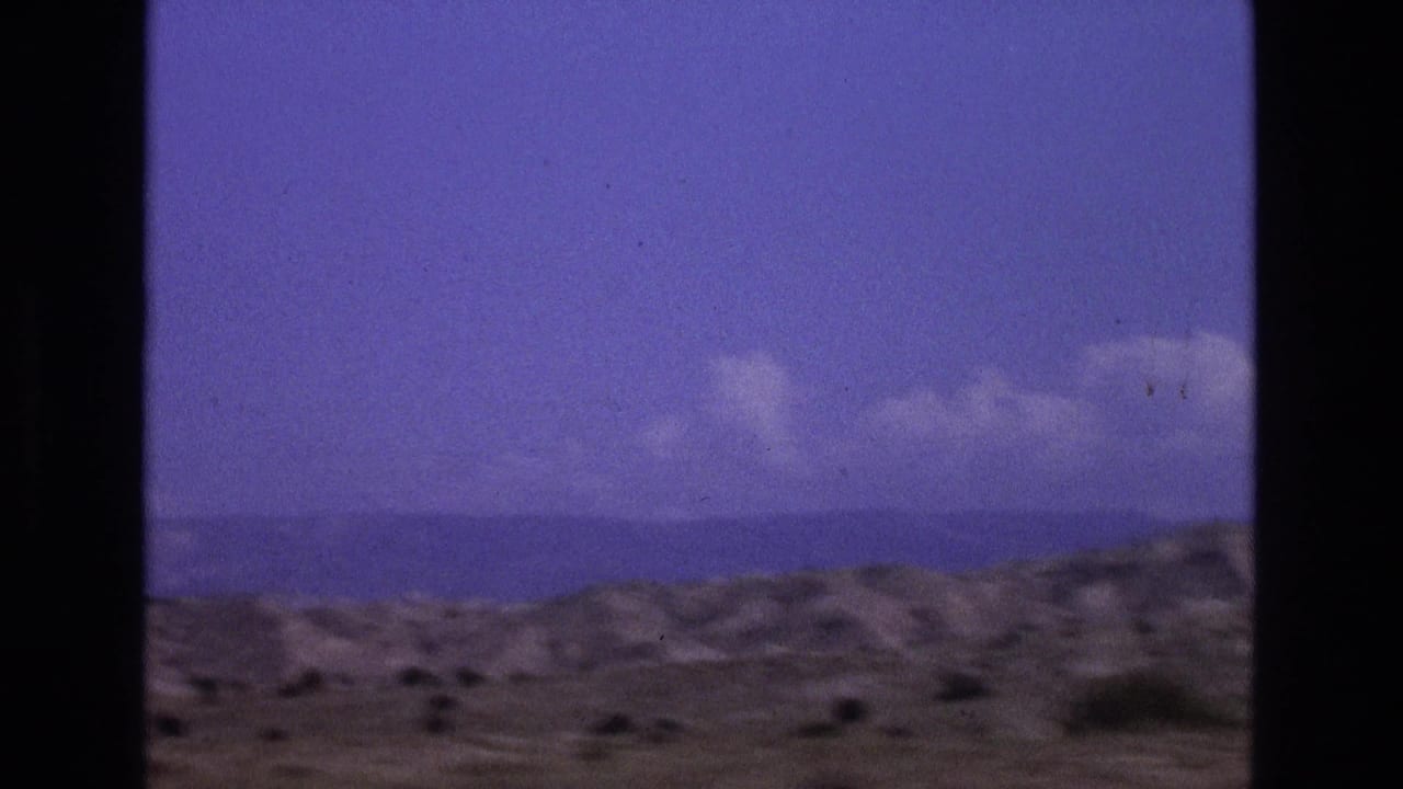 New Mexico desert hills and distant horizon in soft 8mm color, partly blocked by a dark vertical window or vehicle-frame strip.