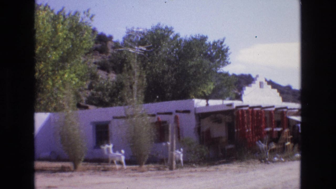 Low white adobe-style building with outdoor chairs, trees, and red chile strings.