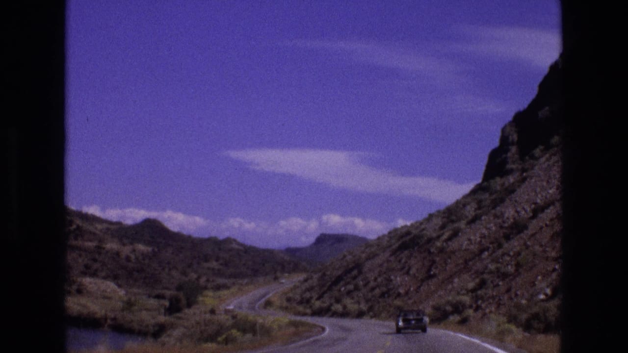 Dark car on a winding desert road beside rocky hills.