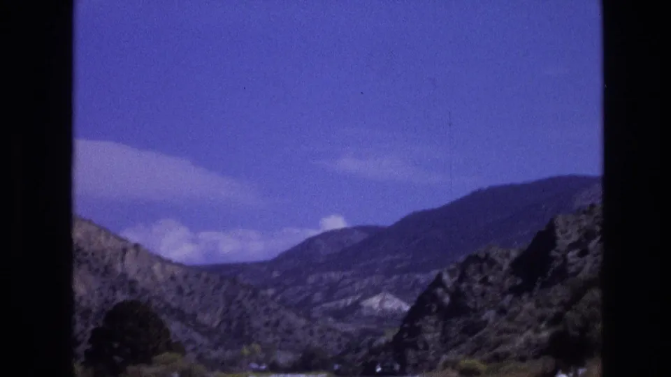 1973 New Mexico 8mm still showing rolling hills and rugged terrain beneath a saturated blue sky, viewed from inside a car.