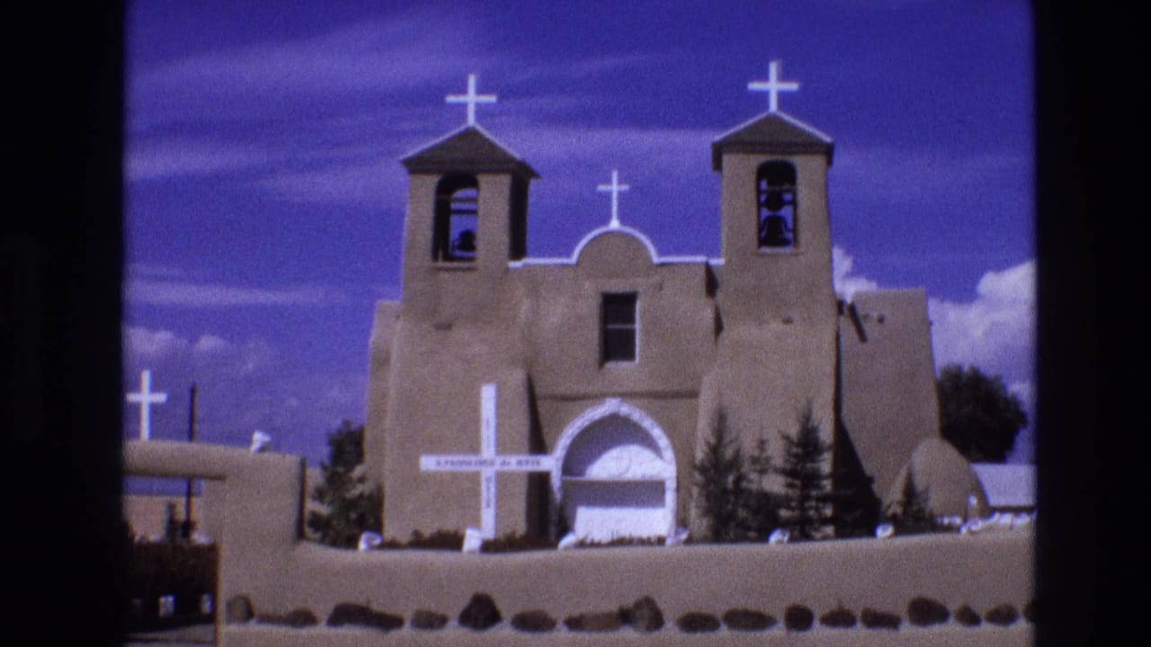 Adobe church exterior with twin bell towers, white crosses, and blue sky.