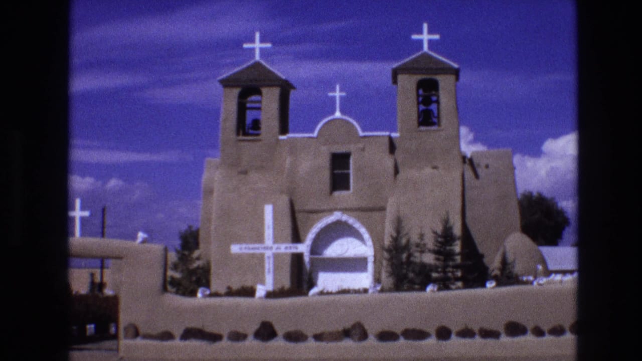 Church exterior with white crosses, bell towers, arched doorway, wall, and clouds.