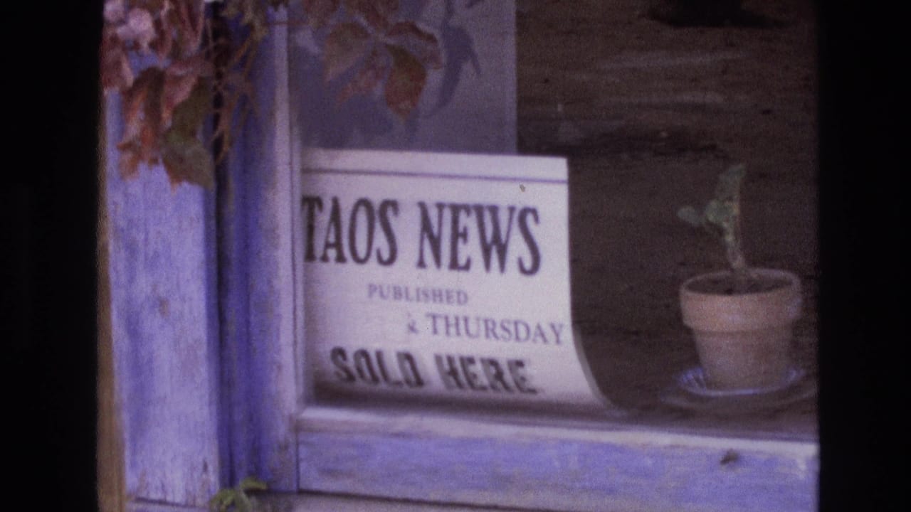 1973 New Mexico 8mm frame showing a storefront window with a Taos News sign, a window ledge, and a small potted plant.