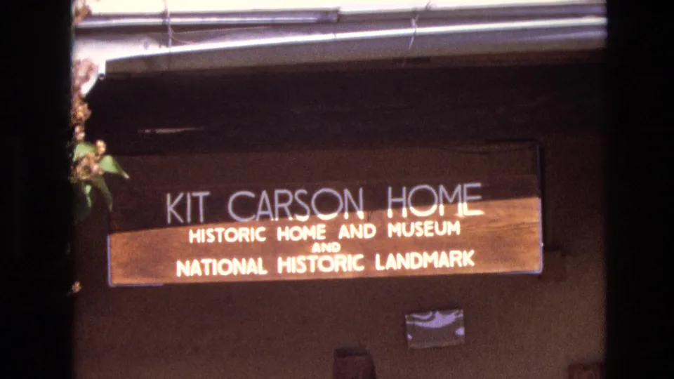 1973 New Mexico 8mm frame showing the Kit Carson Home museum and National Historic Landmark sign from a slightly shifted visitor-shot angle.
