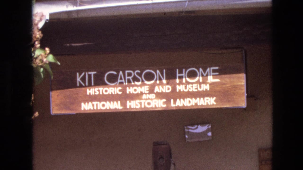 Kit Carson Home sign mounted above a shaded adobe-style building wall.