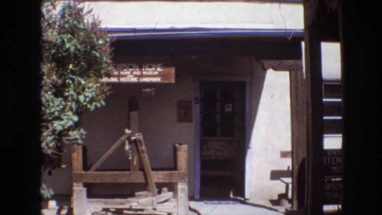 1973 New Mexico visitor footage showing the front of the Carson Home and Museum with a wooden sign, shaded doorway, tree, and rustic well structure.