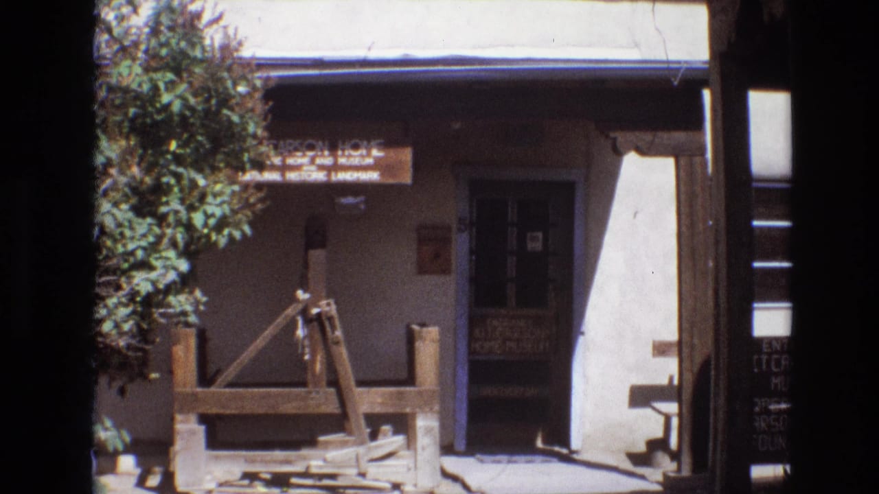 1973 New Mexico frame of the Carson Home and Museum entrance, showing the signboard, shaded doorway, tree branches, and wooden well in front.