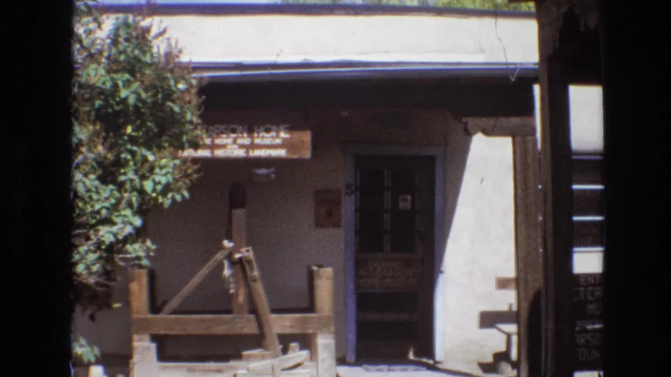 1973 New Mexico frame of the Carson Home and Museum exterior, with the sign above the entrance and a weathered wooden well structure in the foreground.