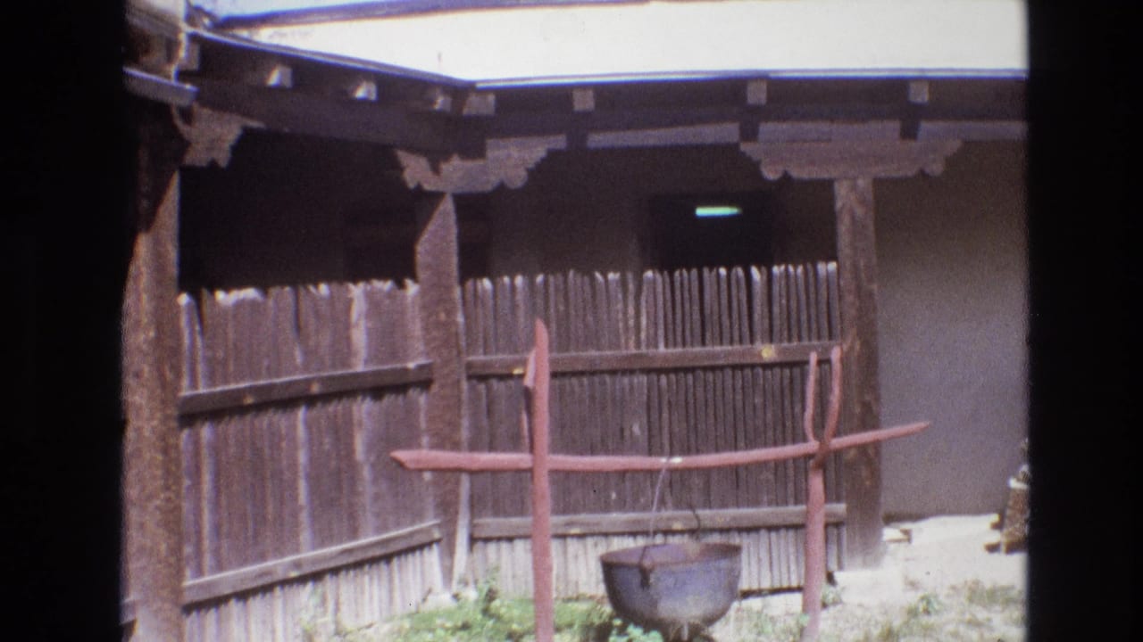 Courtyard fence with a red support frame and hanging pot near a shaded entry.