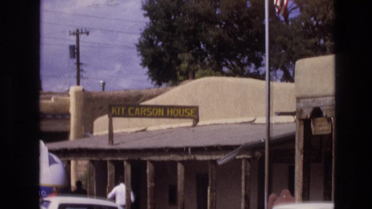 1973 New Mexico frame of the Kit Carson House exterior, with the yellow sign visible above the porch and a person walking near parked cars.