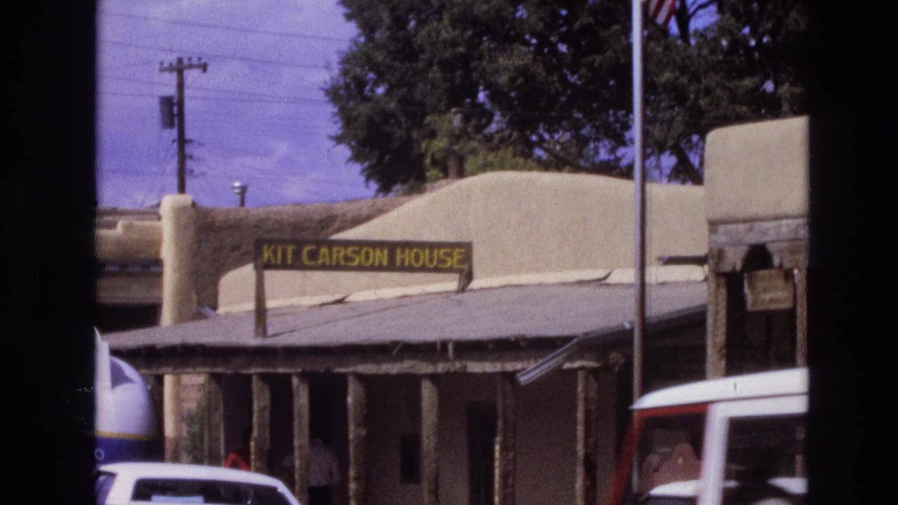 1973 New Mexico 8mm frame showing the Kit Carson House sign on an adobe-style exterior, with utility lines, trees, and vehicles along the street.